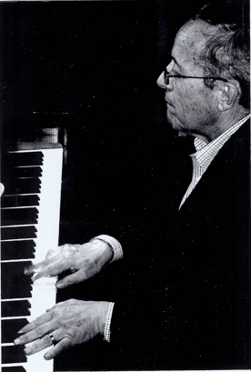 A man playing the piano in front of a black background.